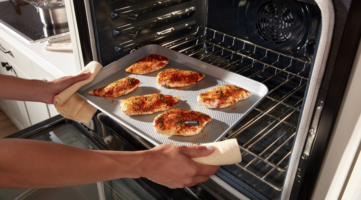 Person pulling a pan of chicken breasts out of an oven