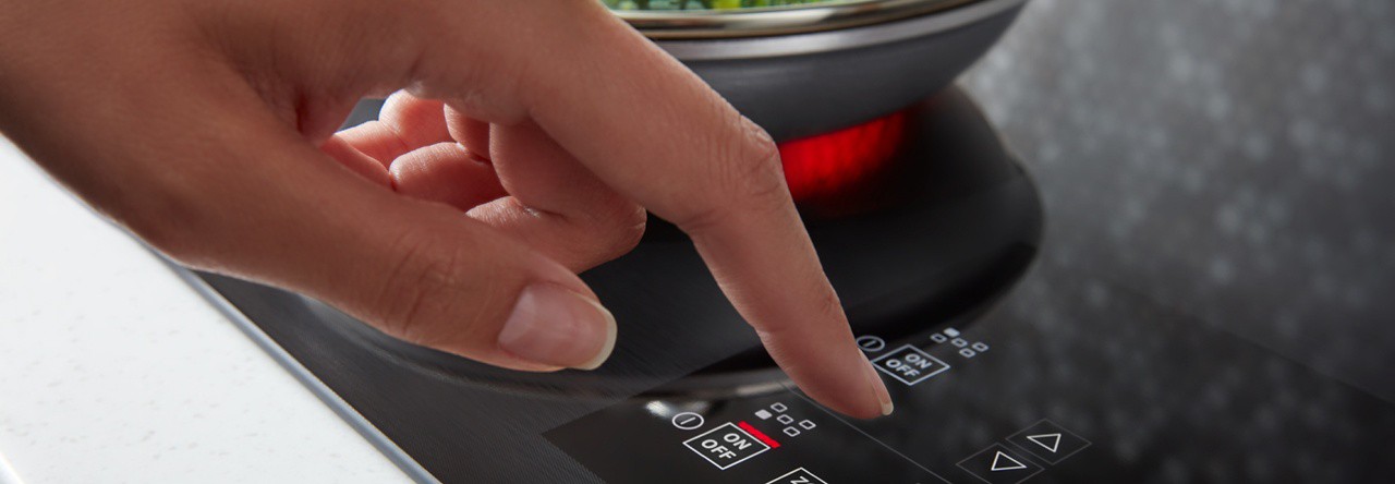 A hand selecting a cooking setting on a stovetop with the latest cooking technology.