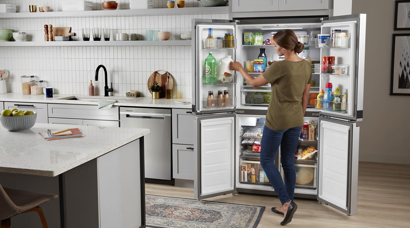 Person stocking the in-door shelving of an open Whirlpool® 4-Door Refrigerator