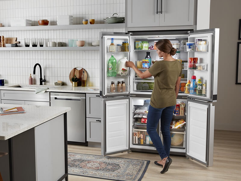 Person stocking the in-door shelving of an open Whirlpool® 4-Door Refrigerator