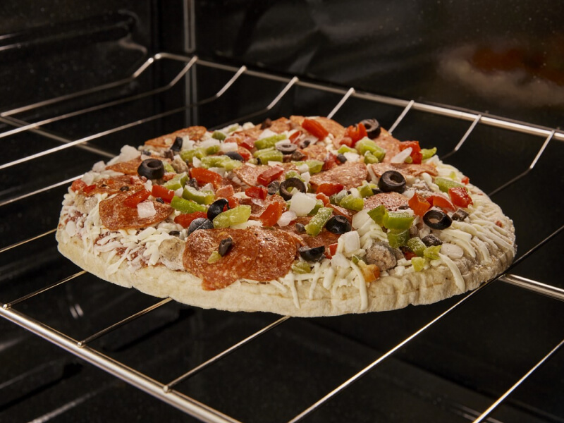 A frozen pizza with vegetables on top cooking in an oven
