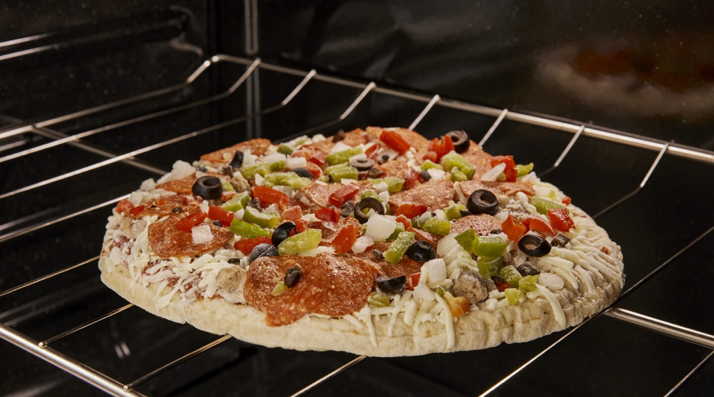 A frozen pizza with vegetables on top cooking in an oven