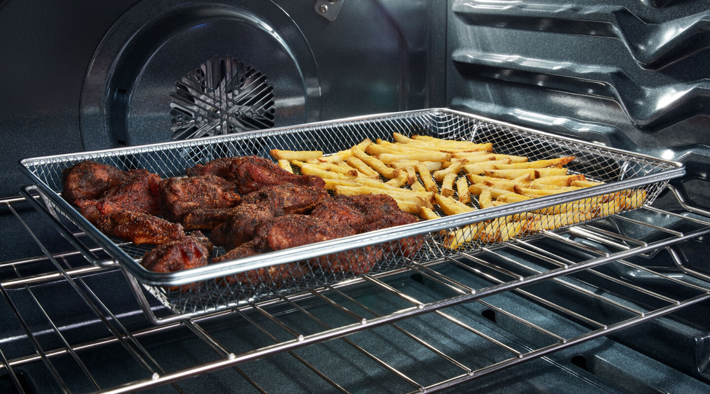 Chicken wings and fries in an air fry basket inside a Whirlpool® oven