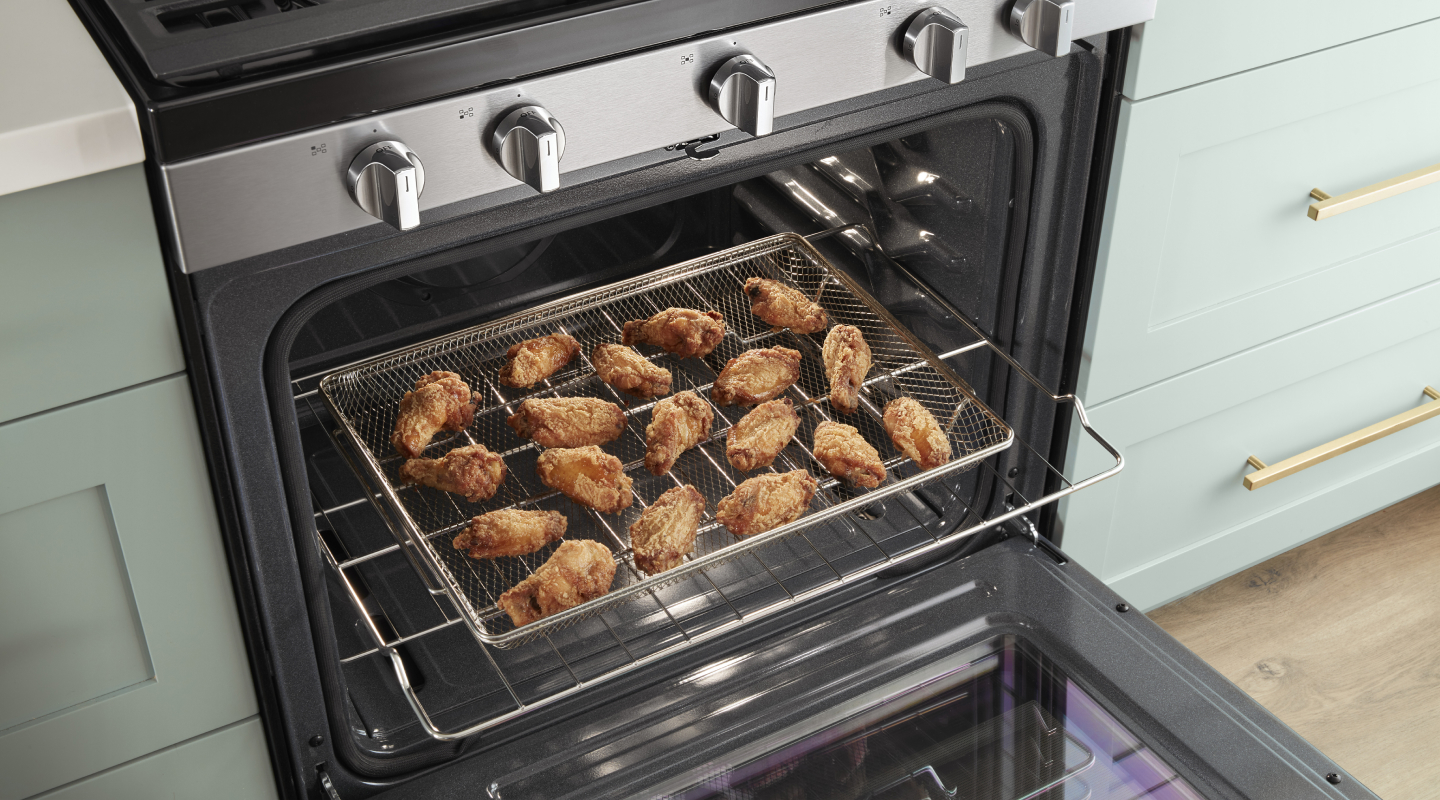 An open oven door with an air fryer basket containing chicken wings slid out.