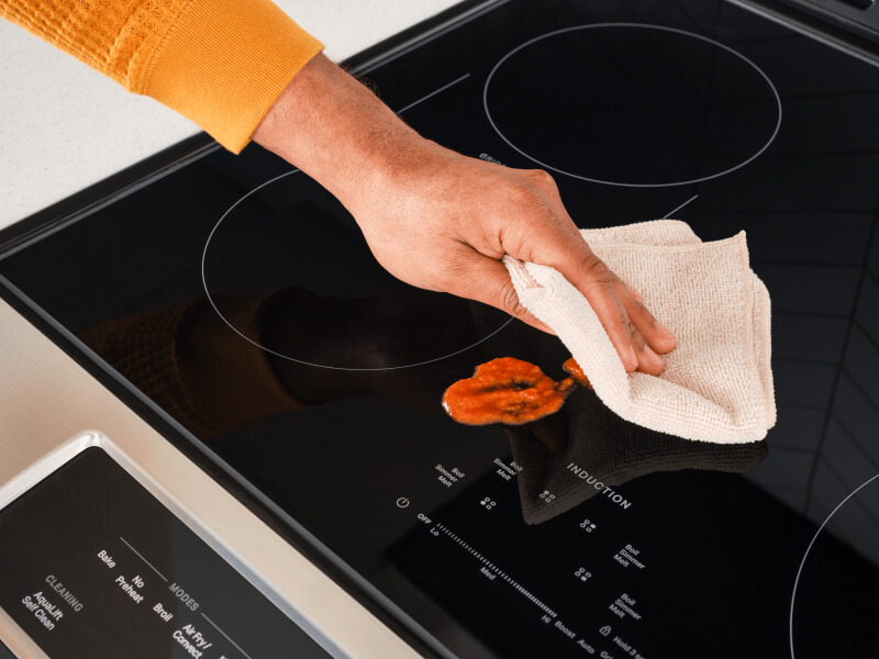 A person cleaning up a spill on an induction cooktop
