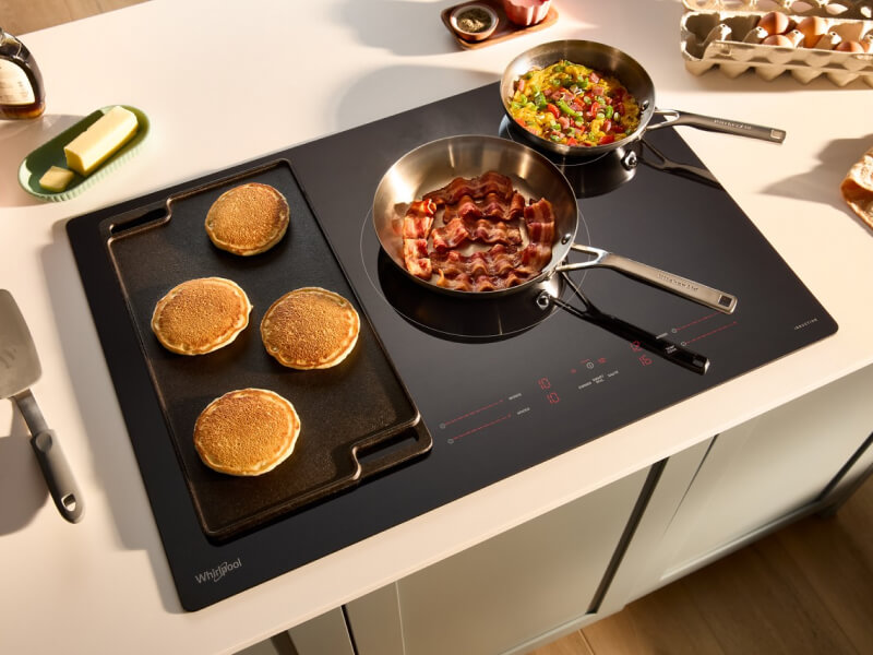 A smooth glass cooktop with pancakes and eggs cooking in pans