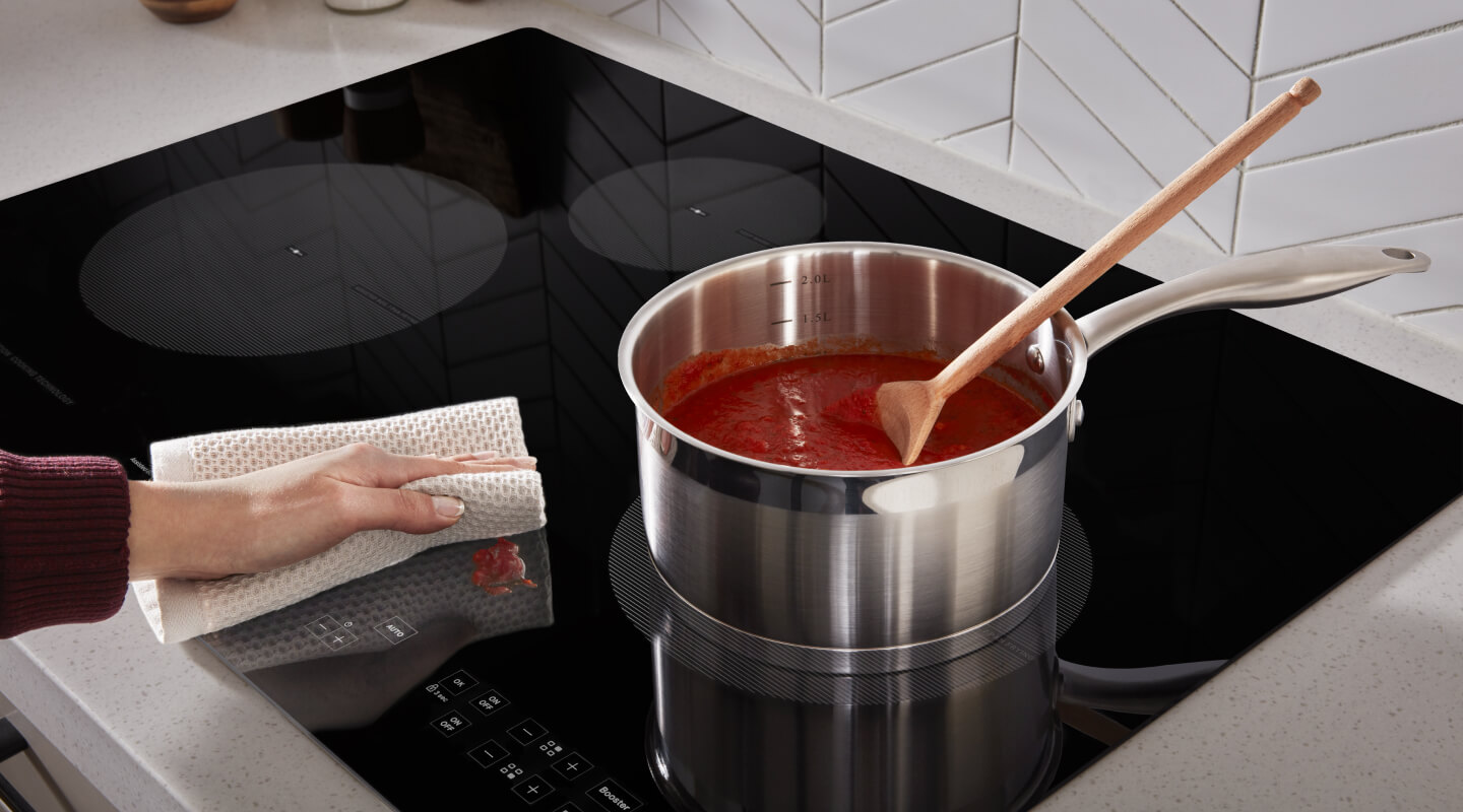 Person wiping cooktop next to burner with saucepan 