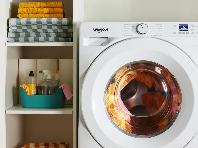 A laundry supply cabinet next to a white washer