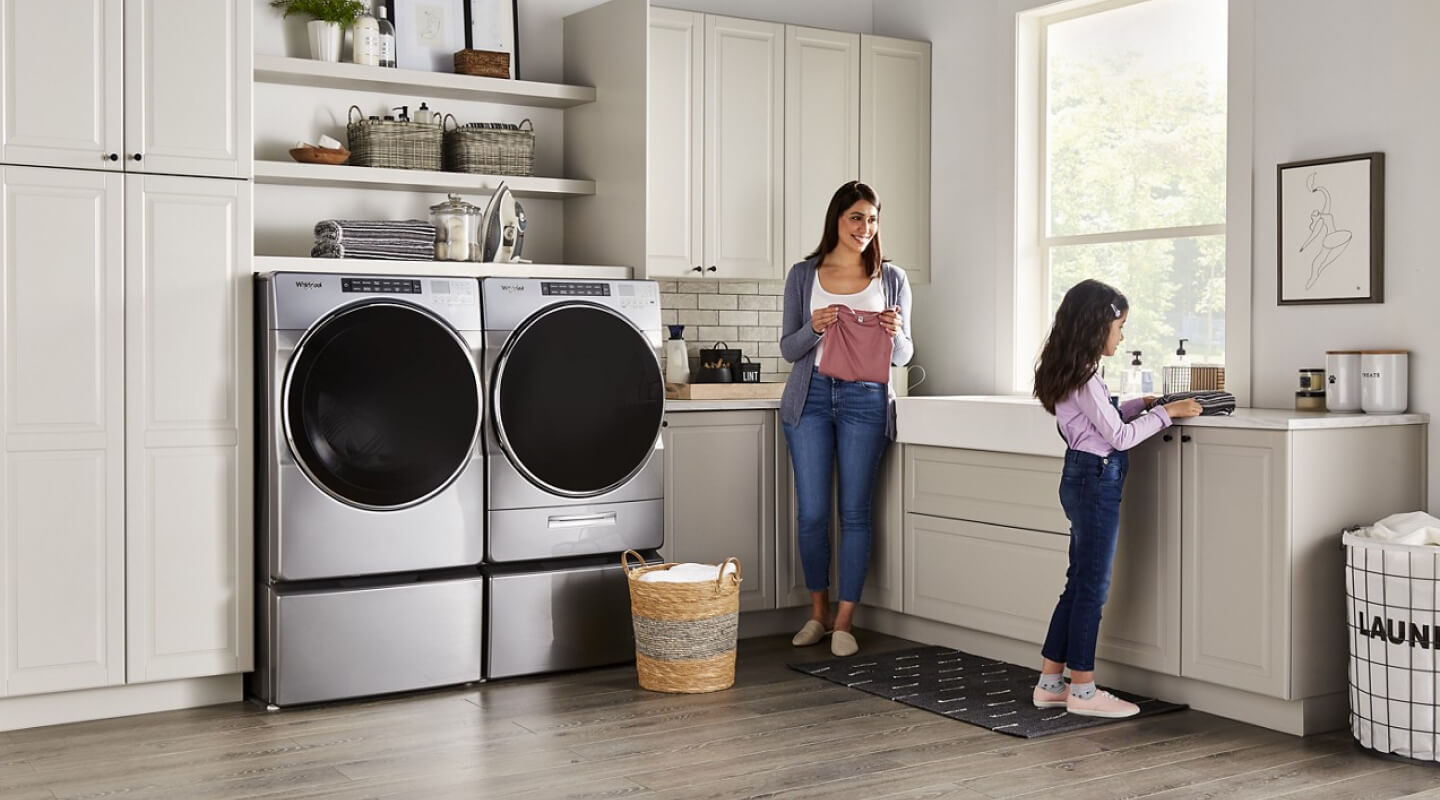 People folding clothes next to a Whirlpool® Washer and Dryer set in a modern laundry room