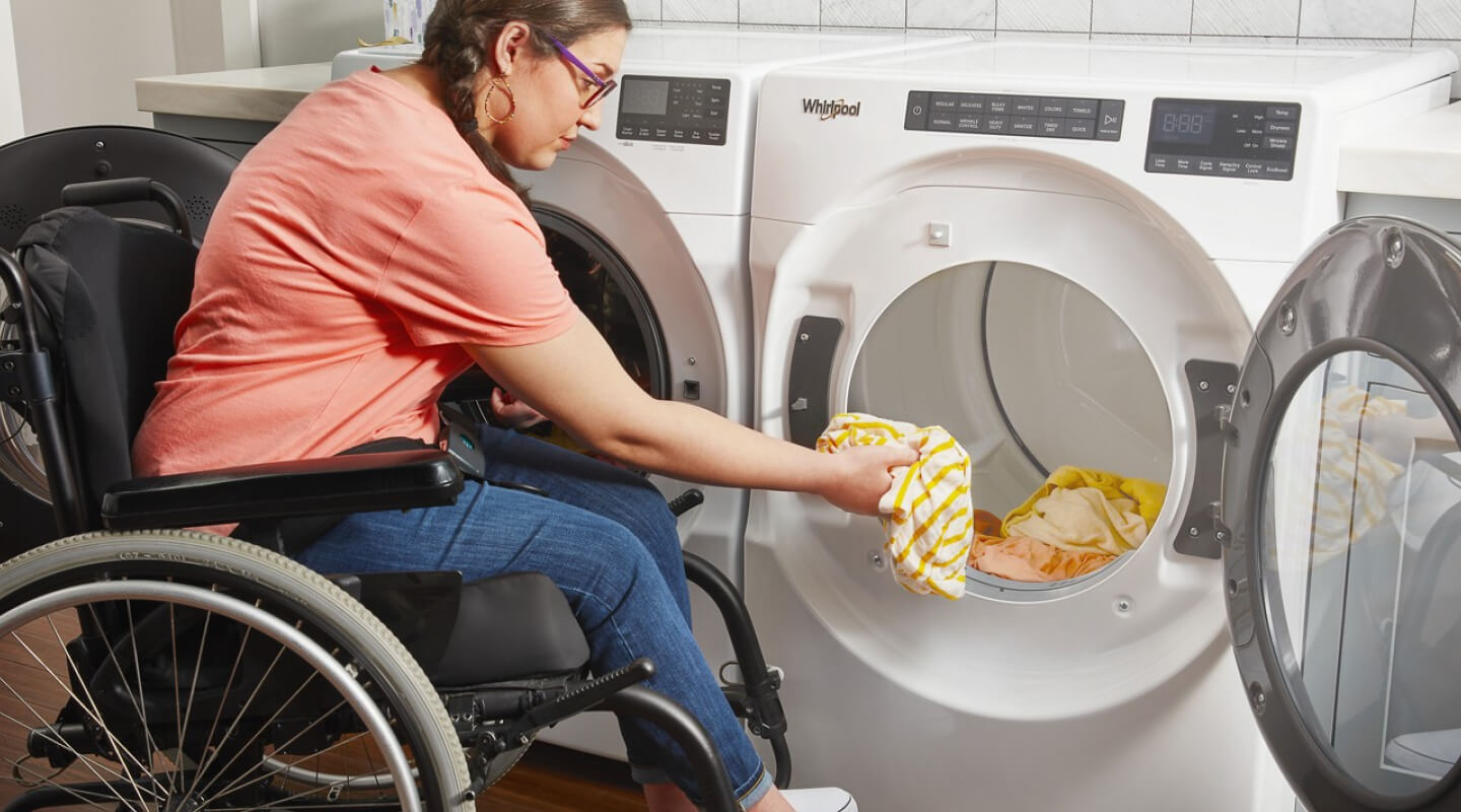 A person in a wheelchair putting clothes into a Whirlpool® Dryer