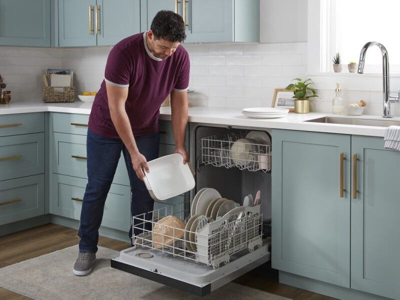 A person loading a Whirlpool® Dishwasher in a modern kitchen