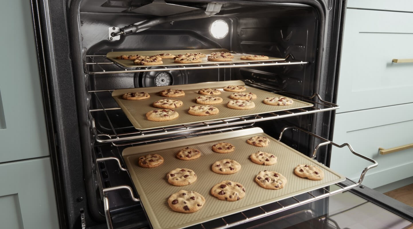 Three trays of cookies baking in an oven