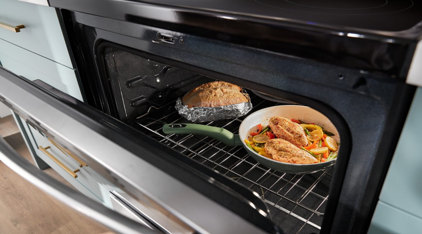 A chicken meal cooking in the oven with a loaf of bread