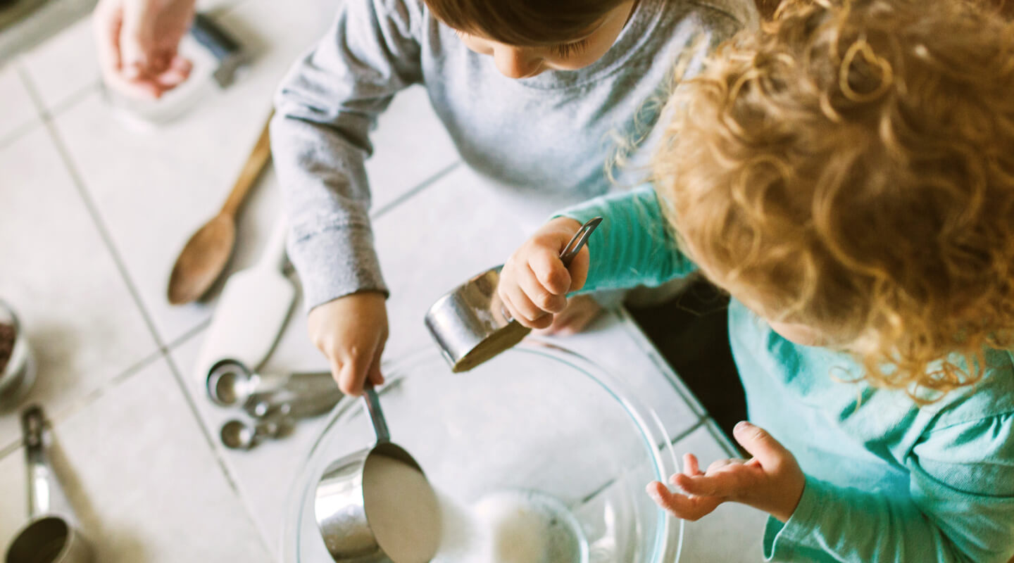 Young children pouring ingredients into a bowl