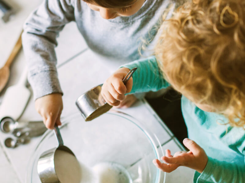 Young children pouring ingredients into a bowl