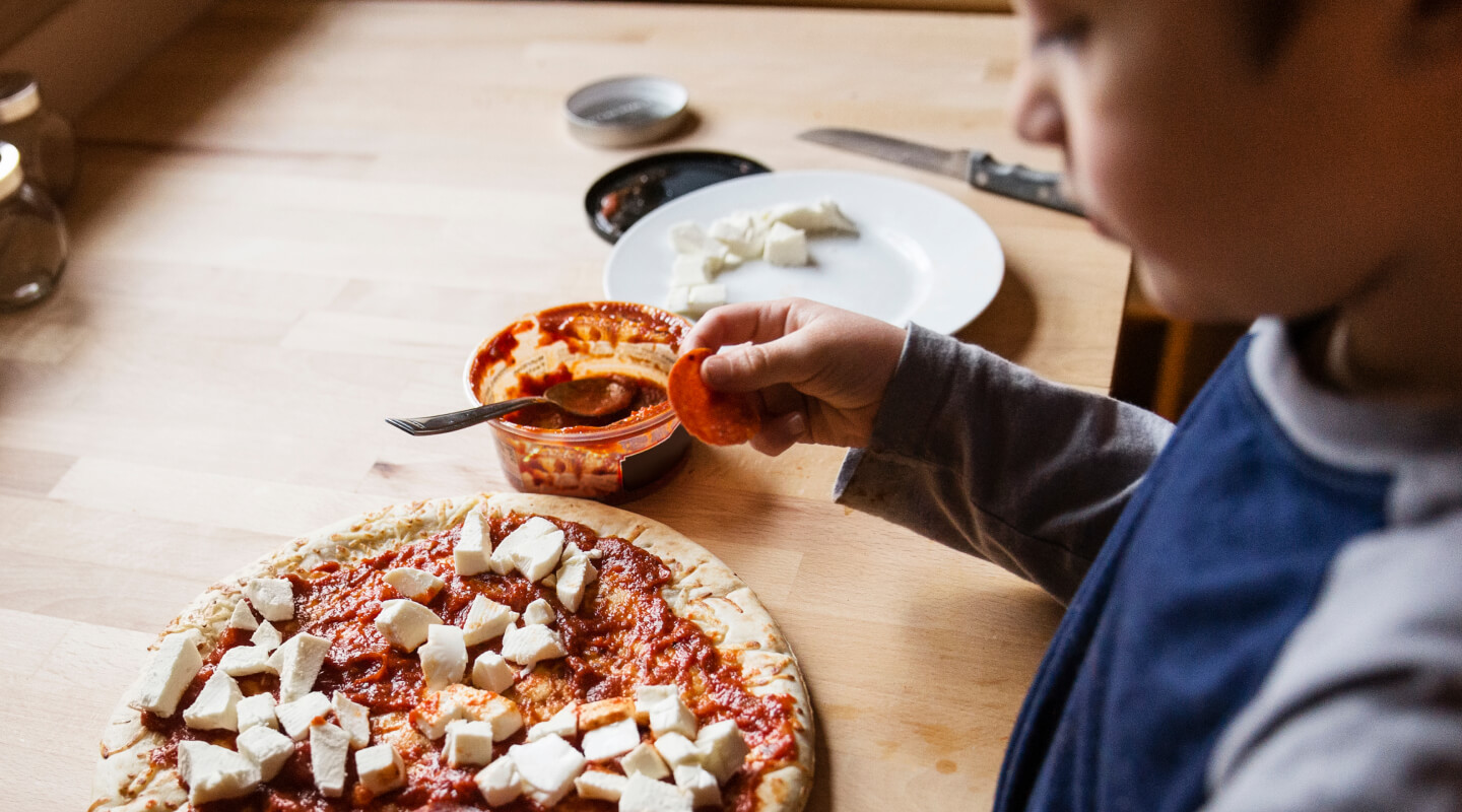 A kid placing toppings on a pizza
