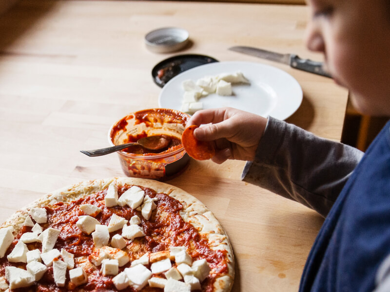 A kid placing toppings on a pizza