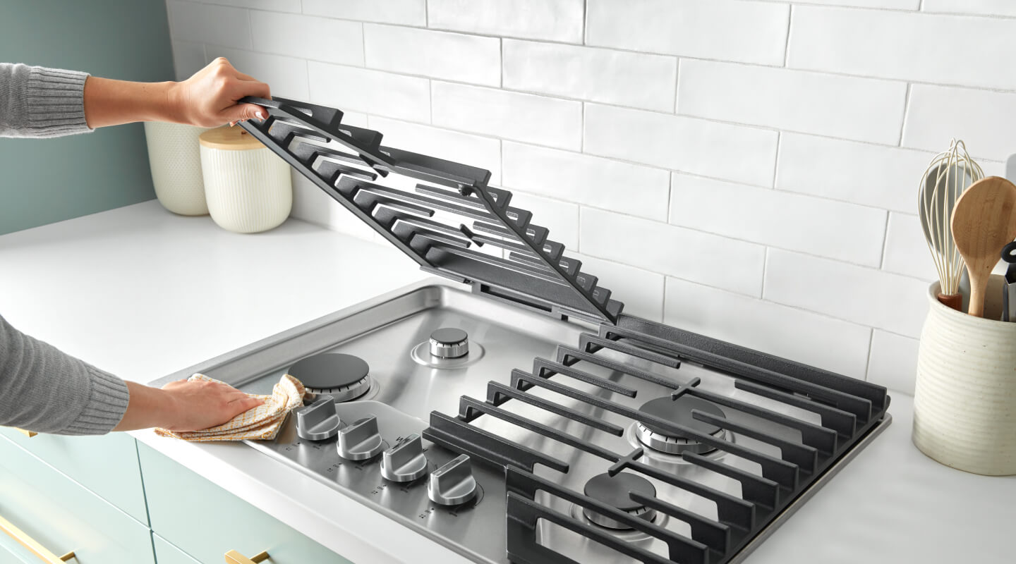 Hand lifting metal grates off of gas cooktop