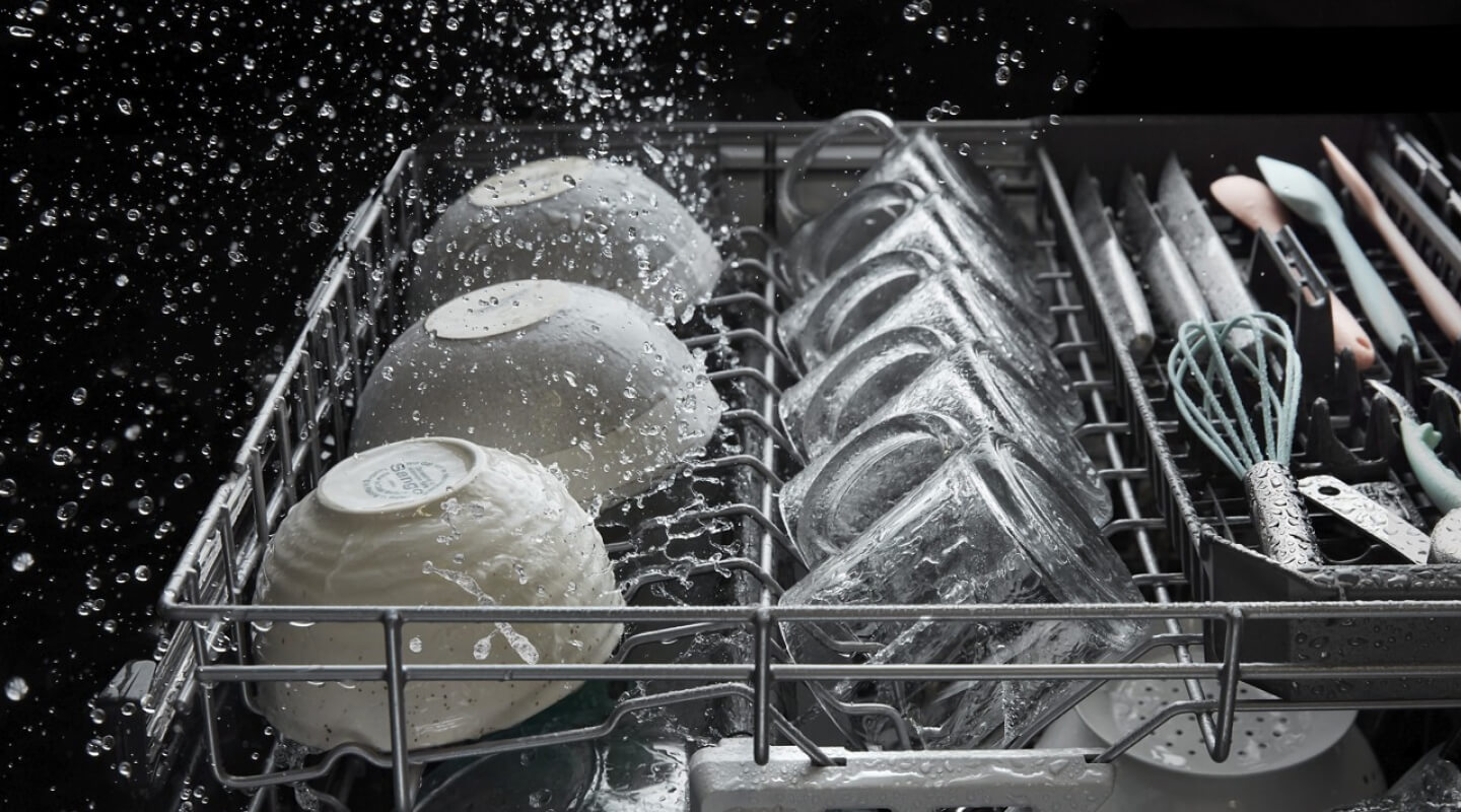 A dishwasher rack of bowls and mugs in the middle of a wash cycle
