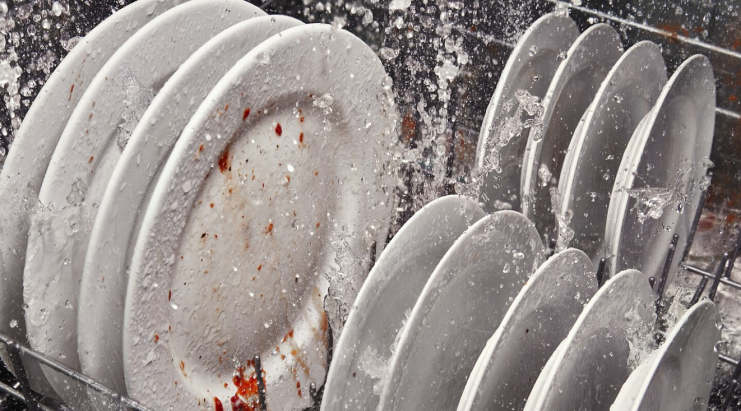 A rack of dirty dishes in the middle of a wash cycle