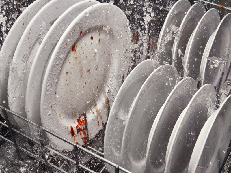 A rack of dirty dishes in the middle of a wash cycle