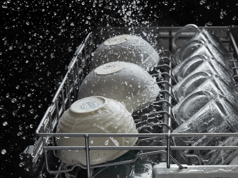 A dishwasher rack of bowls and mugs in the middle of a wash cycle
