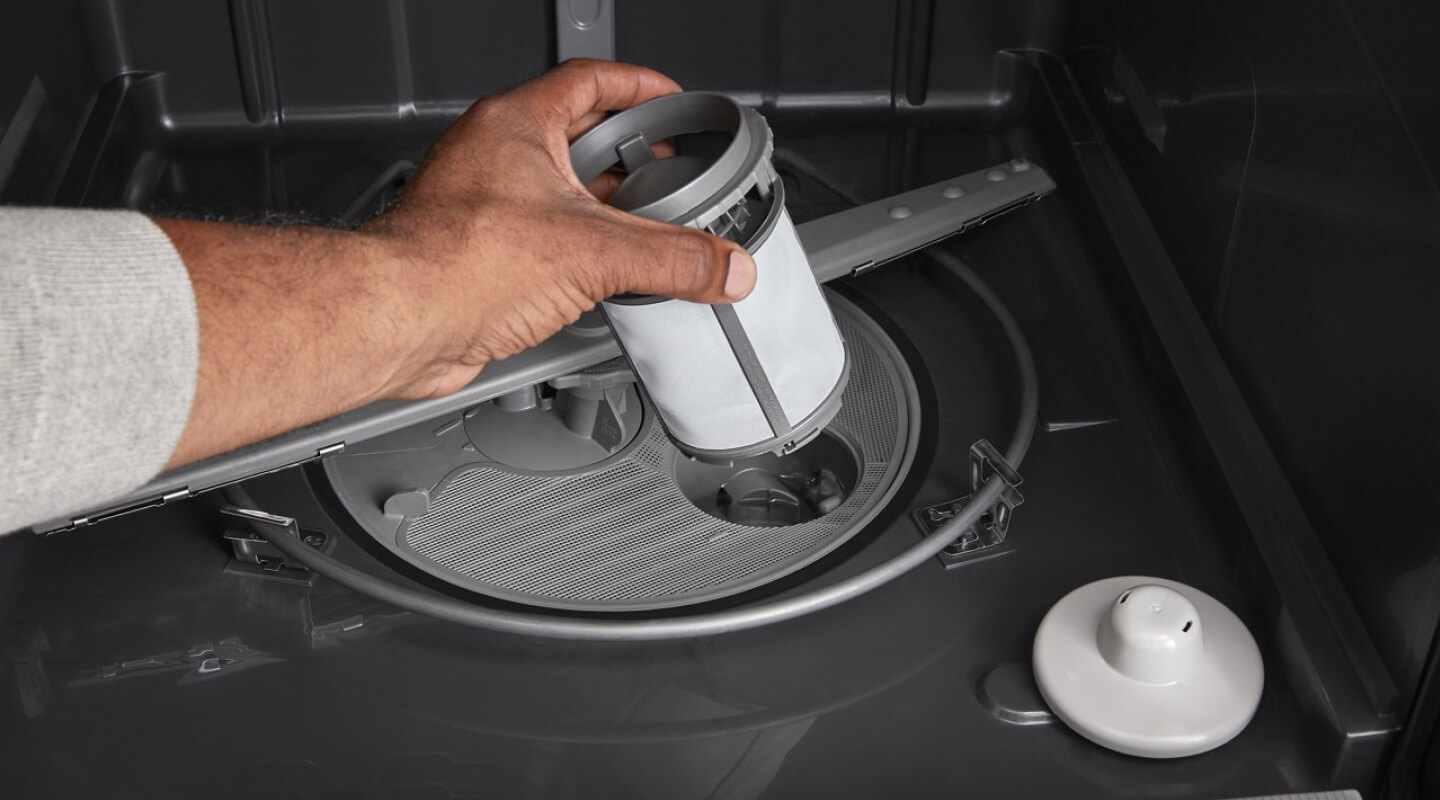 A person pulling a filter out of a dishwasher