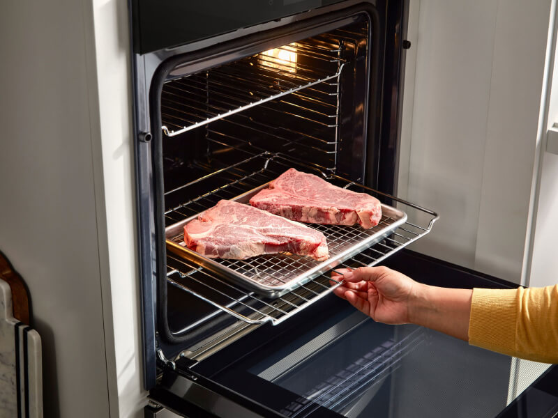 Person putting two steaks in a Whirlpool® wall oven