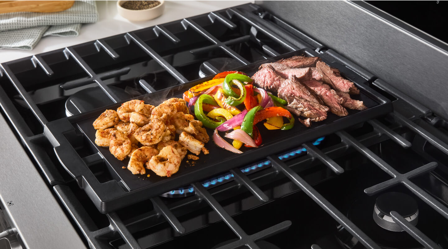 Meat and vegetables cooking on a stovetop griddle