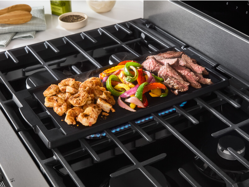 Meat and vegetables cooking on a stovetop griddle