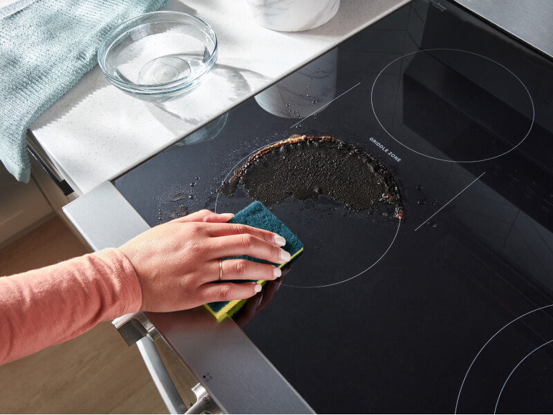 Person cleaning a spill on an electric cooktop