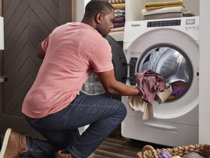 Person loading laundry into a white Whirlpool® Front Load Washer