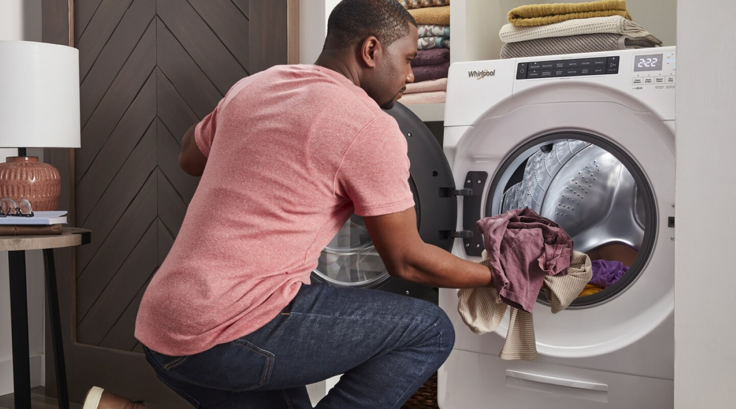Person loading laundry into a white Whirlpool® Front Load Washer