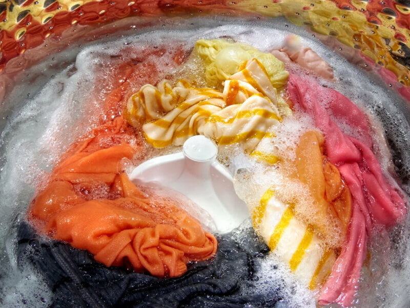 Colorful laundry load soaking inside of a top load washer with an agitator