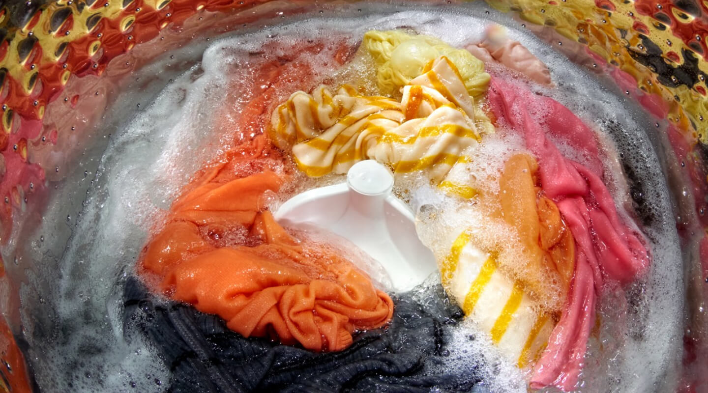 Colorful laundry load soaking inside of a top load washer with an agitator