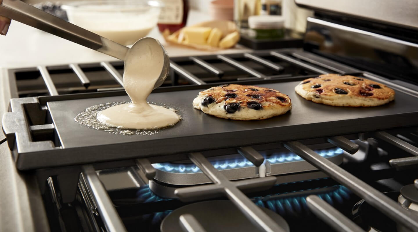 A person making blueberry pancakes on a griddle on top of a Whirlpool® Gas Range cooktop