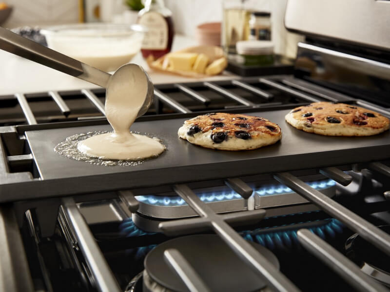 A person making blueberry pancakes on a griddle on top of a Whirlpool® Gas Range cooktop