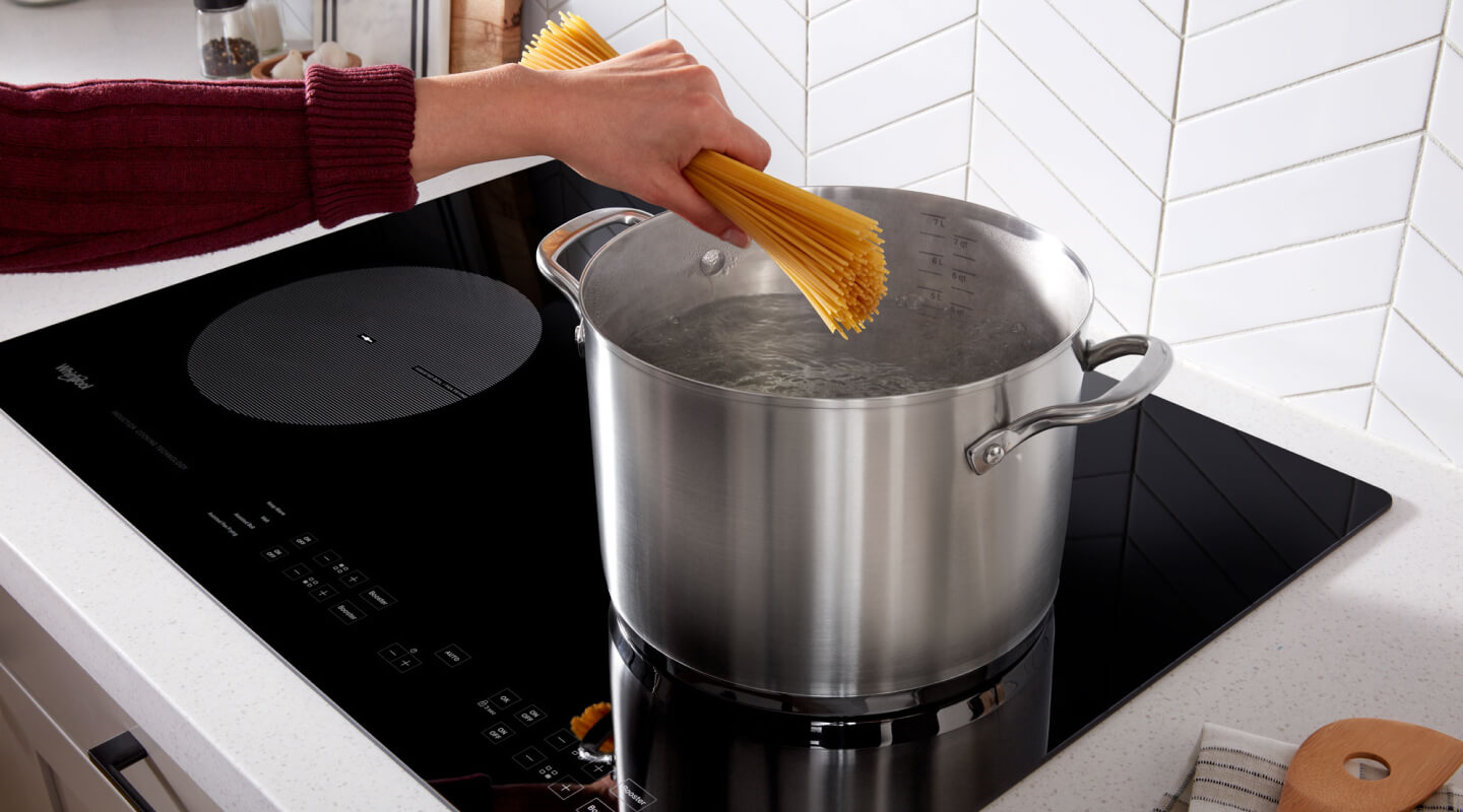 Someone putting spaghetti into a pot of water on an induction cooktop