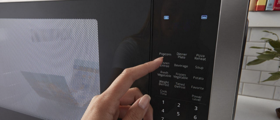 A hand selecting a popcorn setting on a microwave
