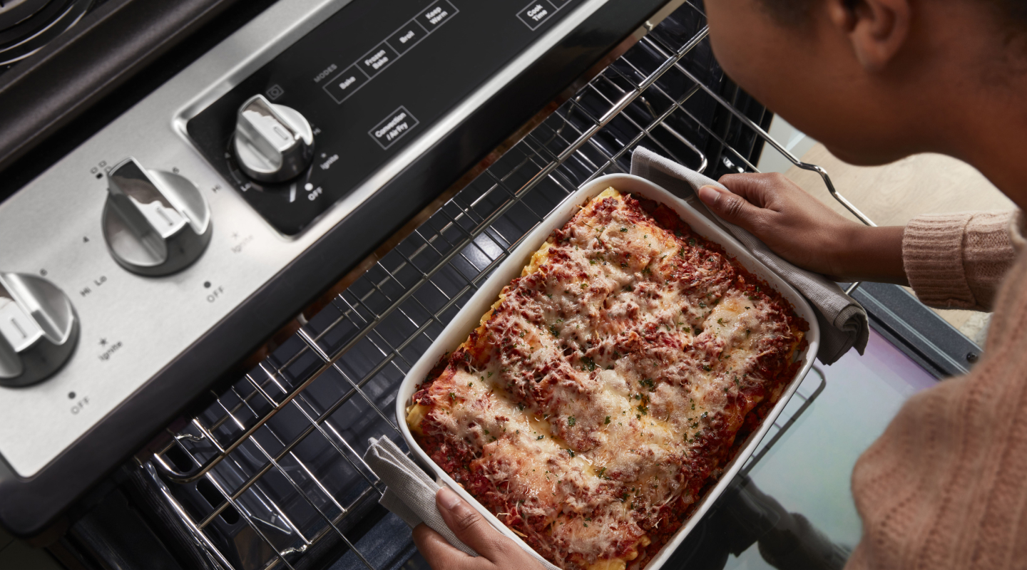 Top view of a person pulling casserole out of the top rack of an oven