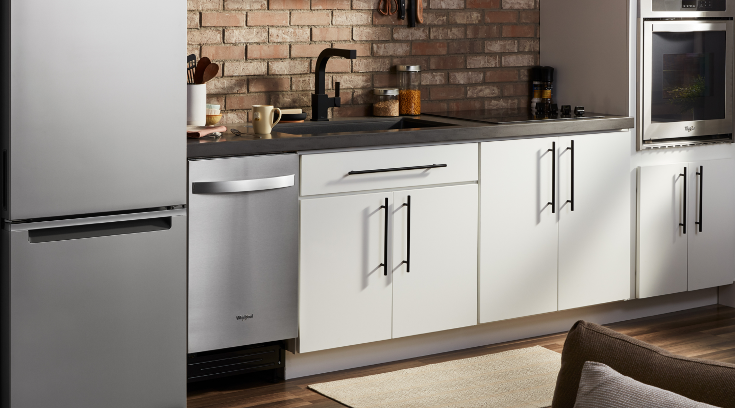 A stainless steel Whirlpool® dishwasher, refrigerator and oven in a modern kitchen.
