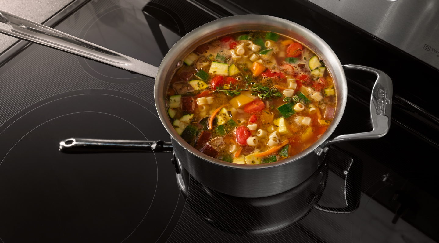 A pot of vegetable soup on a ceramic glass stovetop.