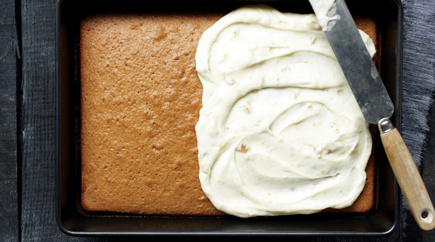 A pan cake with frosting on the right half and a knife balanced on top