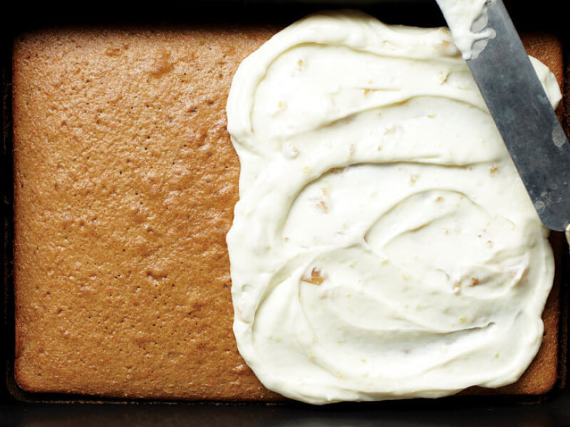 A pan cake with frosting on the right half and a knife balanced on top