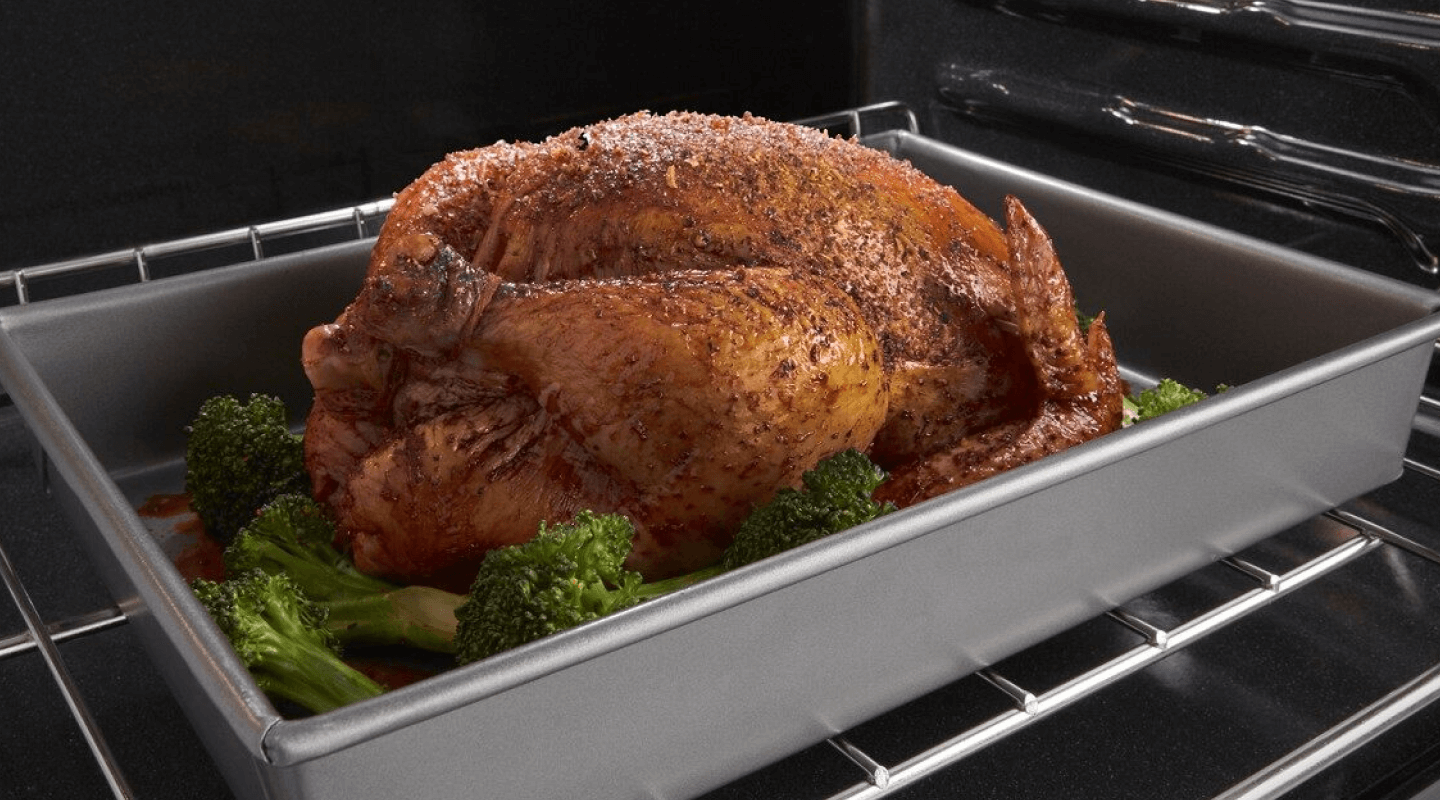 Seasoned cooked turkey in a roasting pan surround by stalks of broccoli