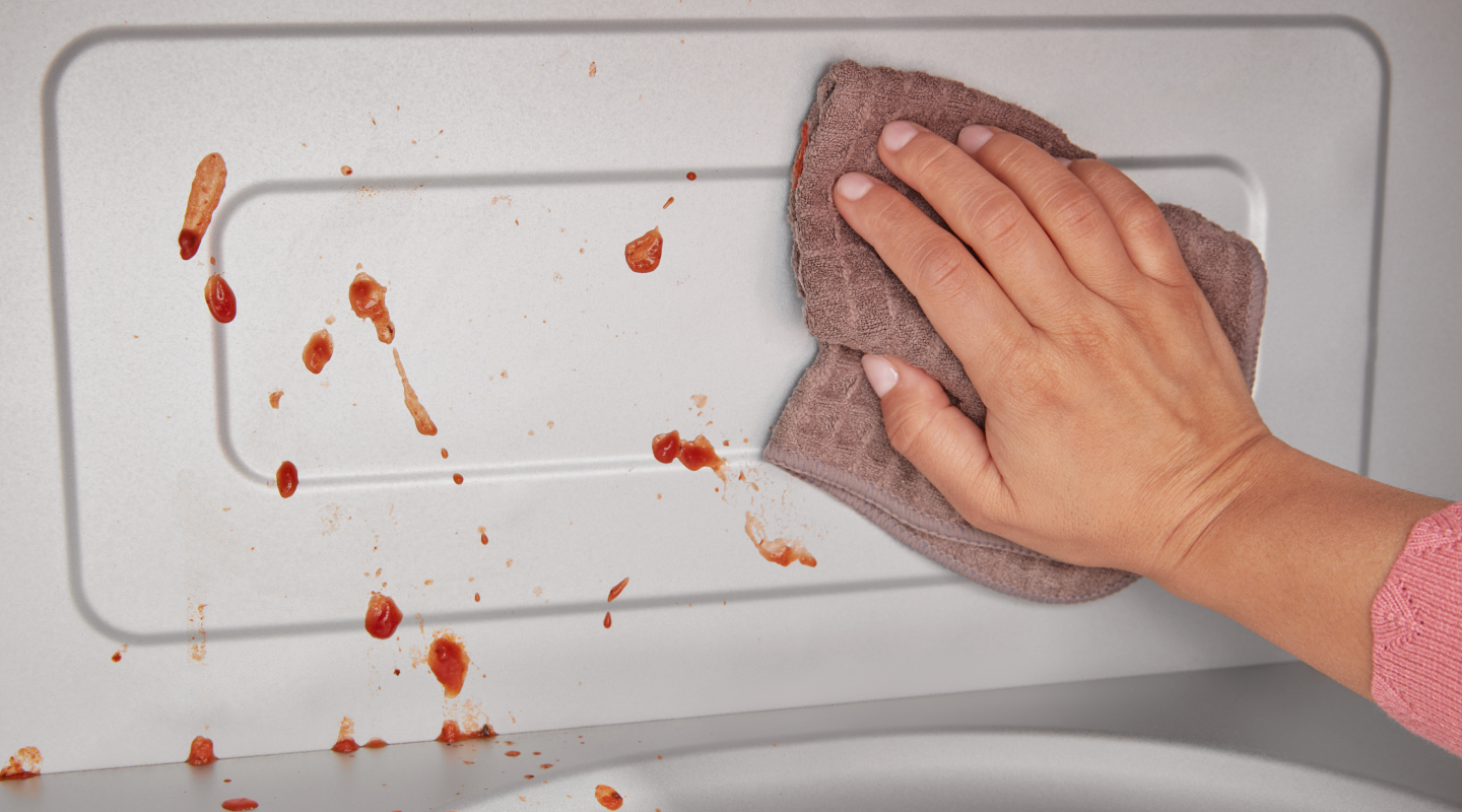 Person wiping splatters from microwave interior with rag