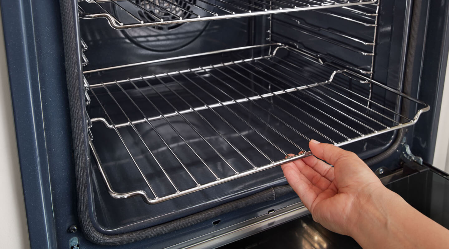 A hand sliding the bottom rack of an oven into place