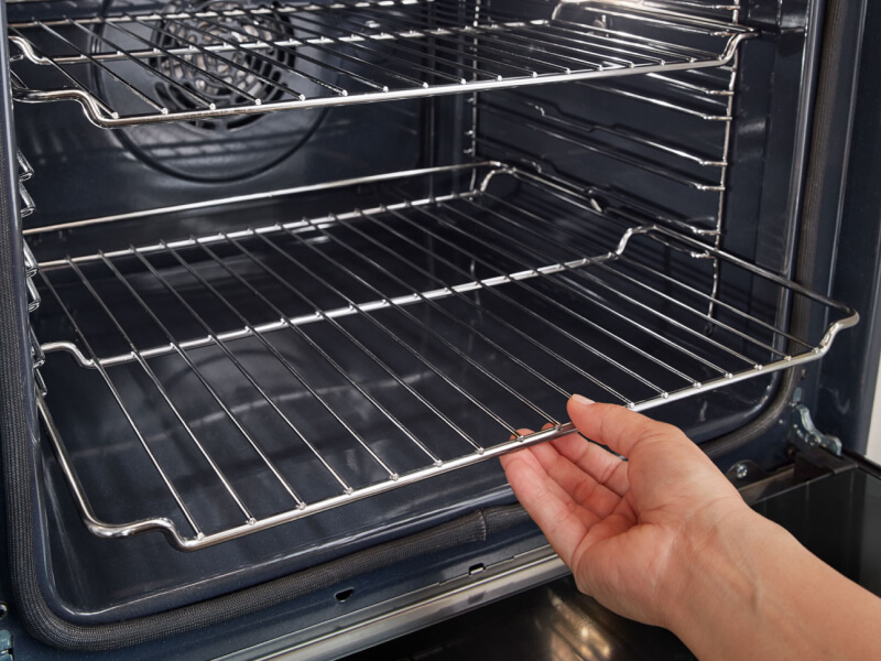 A hand sliding the bottom rack of an oven into place