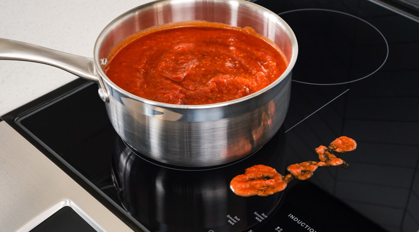 Sauce in a pan on an induction stovetop, next to splatter on the stovetop