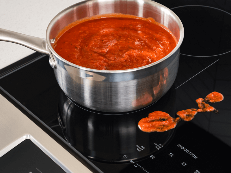 Sauce in a pan on an induction stovetop, next to splatter on the stovetop